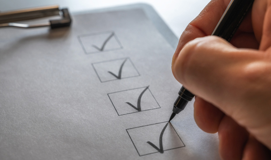 A hand holding a pen marks off checklist on a clipboard