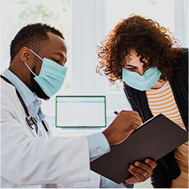 Doctor and patient both wearing masks, reviewing notes on a clipboard