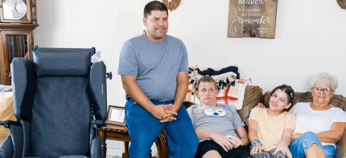 A family impacted by Huntington's Disease sits on the sofa next to a Broda wheelchair