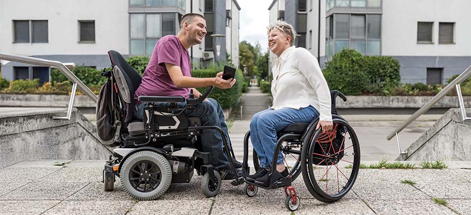 Two friends. in different types of wheelchairs mingling outside