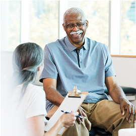 Female caregiver with clipboard talking to a seated elderly man