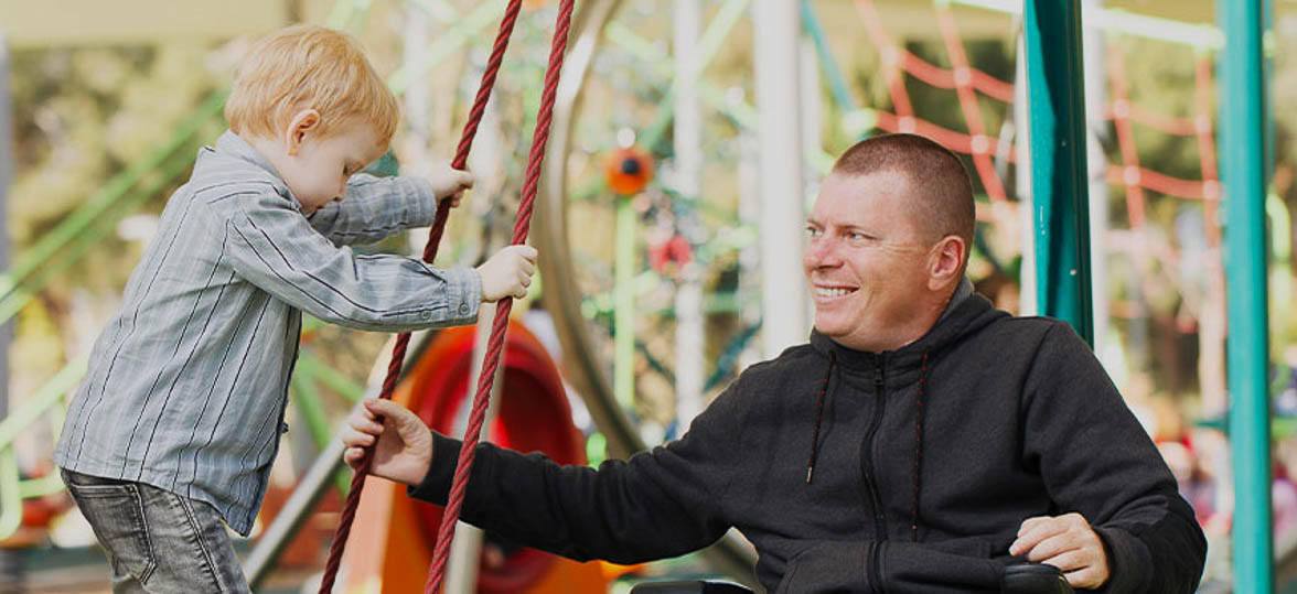 A father in a wheelchair playing with his child at a park