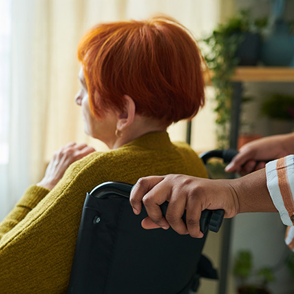 Elderly woman in a wheelchair looking out the window with a caregiver behind her